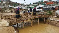 Women walking over a bamboo bridge in a refugee camp.