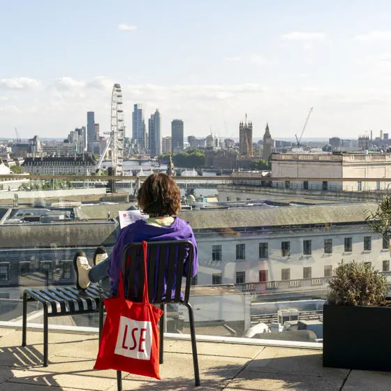 Student sitting on chair on rooftop terrace facing london eye