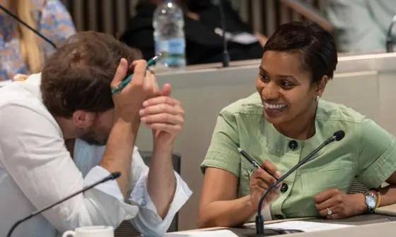 Two professionals in discussion during a seminar, smiling and taking notes in a classroom setting.