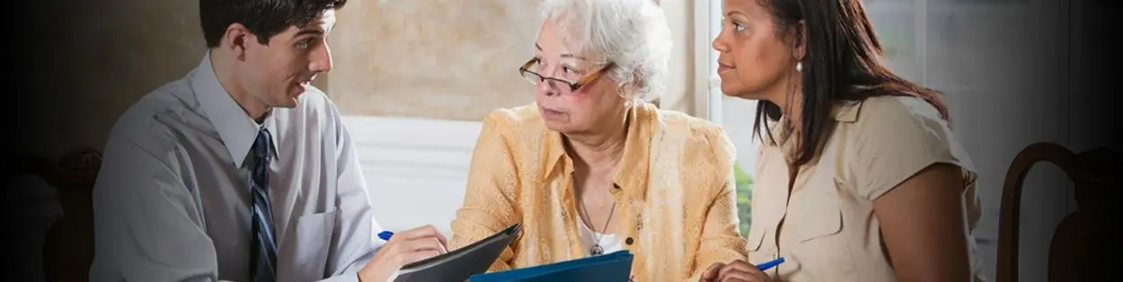 A man in a suit talking with an elderly woman and another younger woman going through paperwork.