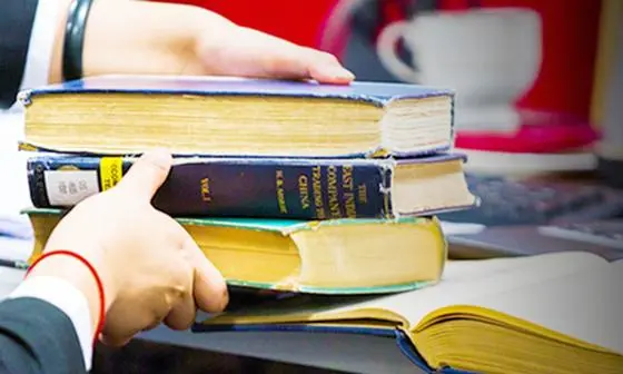 Student lifting pile of books from desk