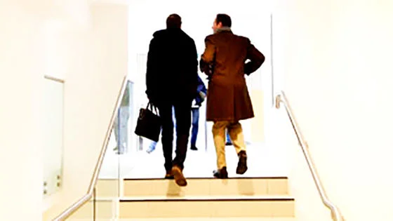 Two men walking up a stairway, one carrying a bag