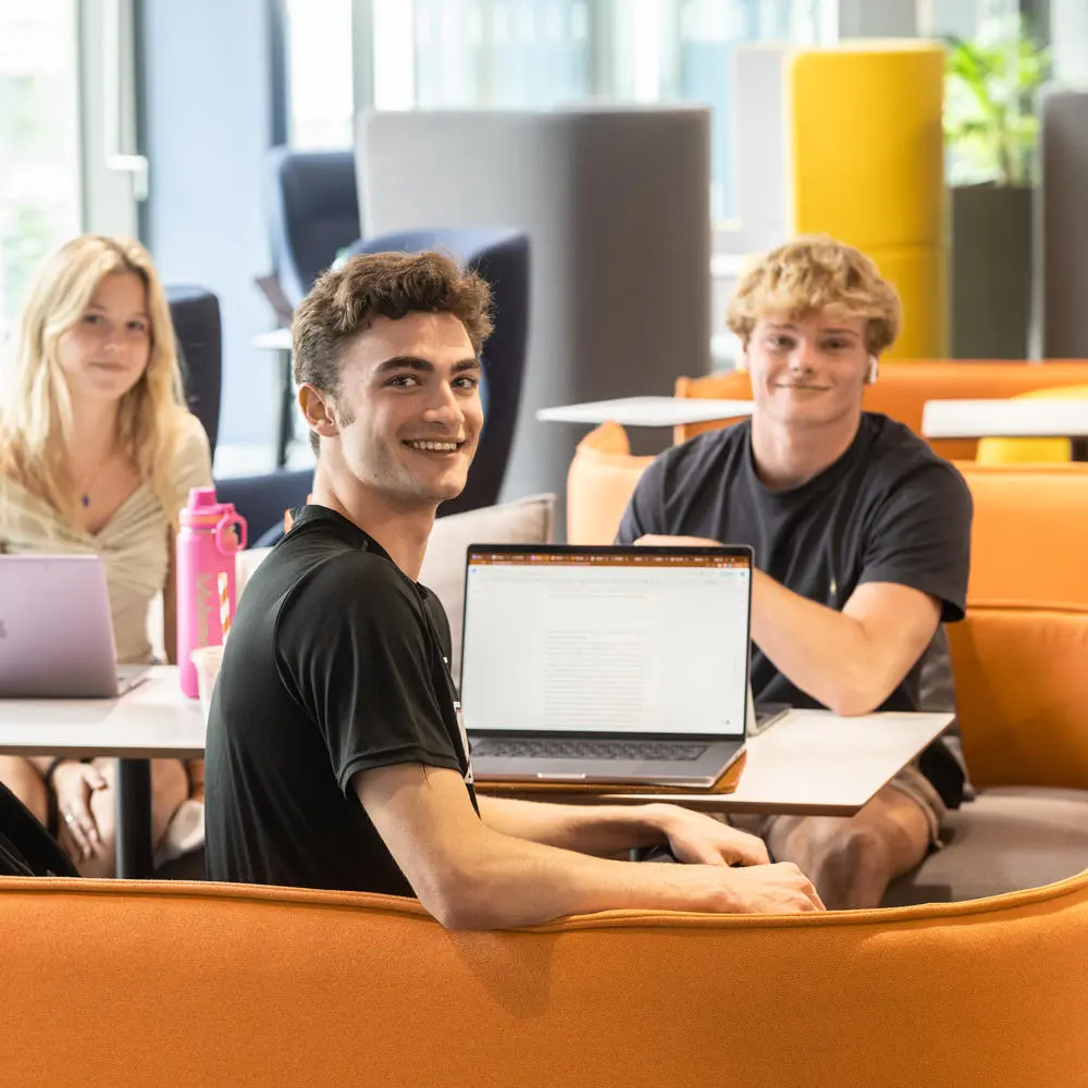 A group of smiling students with laptops sat at a table