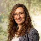 woman smiles at the camera with a background image of foliage behind her