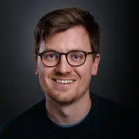 Headshot of Will Kendall, he is smiling against a grey backdrop and wearing glasses.