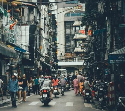 People walking on a rad between buildings, with heavy motorcycle traffic.