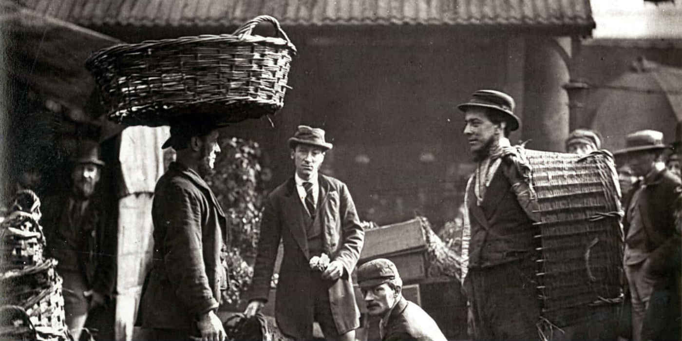 A group of labourers in Victorian London. Some appear to be carrying baskets with one of the labourers carrying a basket on their head.