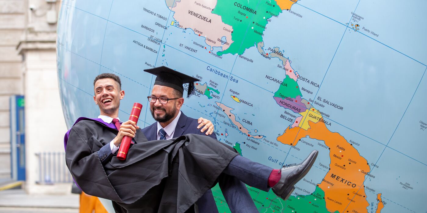 Two students in graduation gowns in front of LSE's globe
