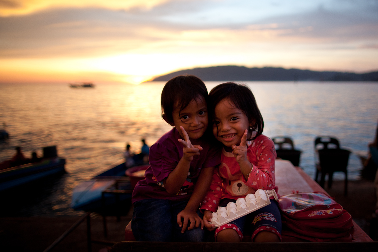 Two children doing peace signs by the sea at sunset
