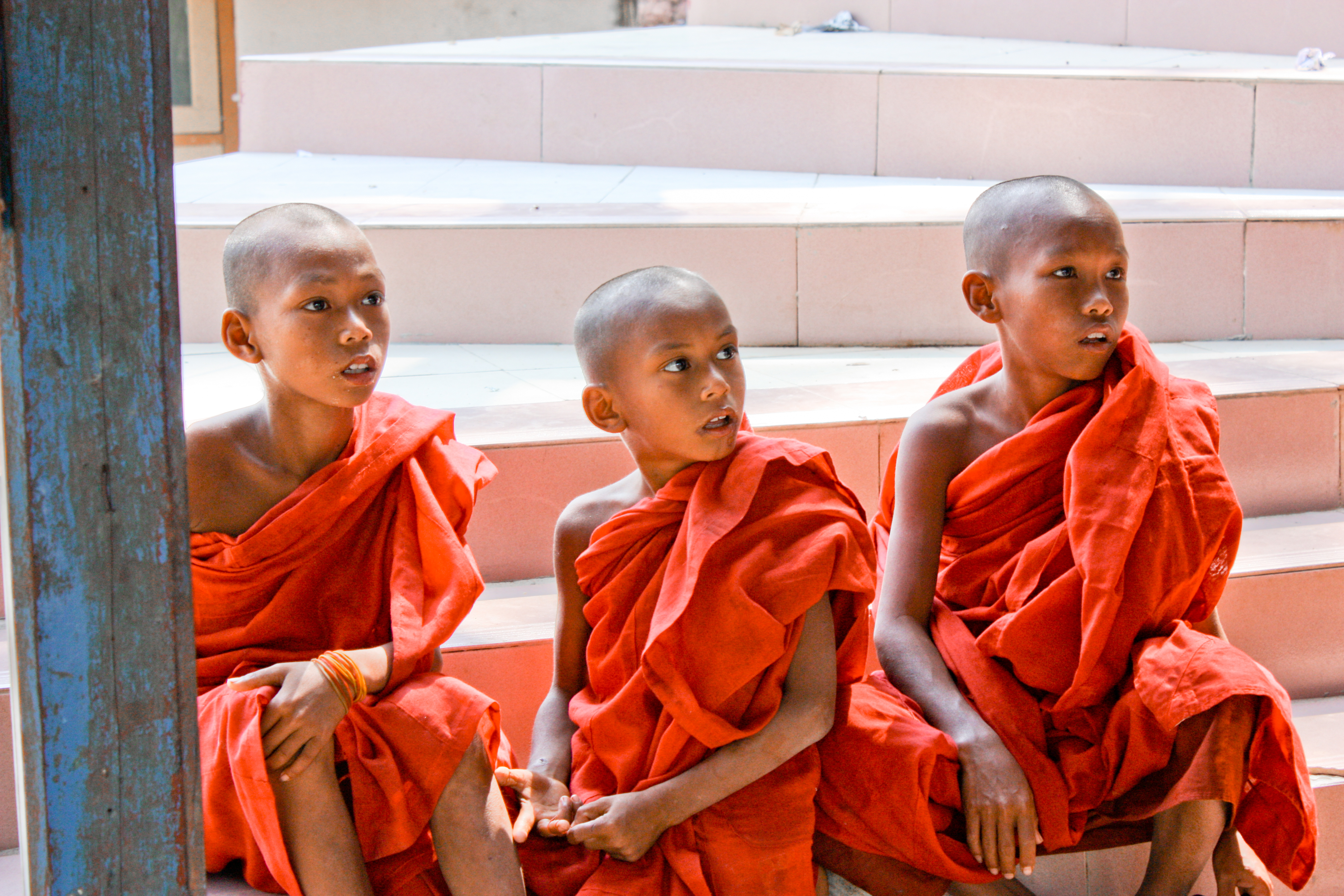 Three young monks in orange robes sitting on some stairs