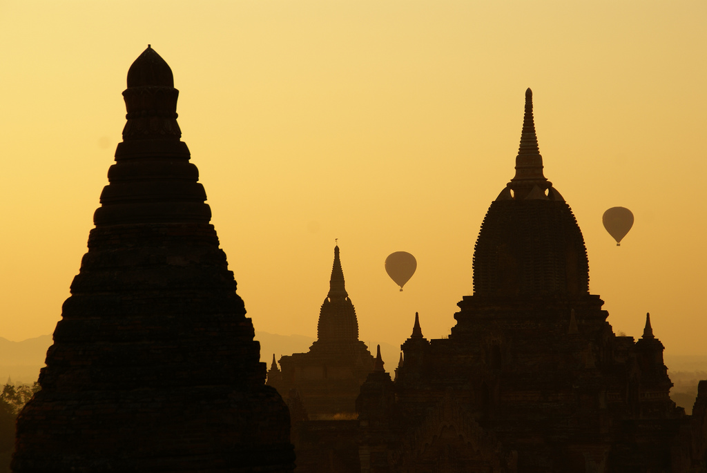 Three temples and two hot air balloons silhouetted against a yellow sky