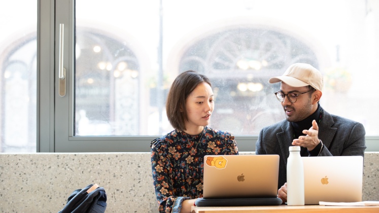 Two students working on laptops in front of window