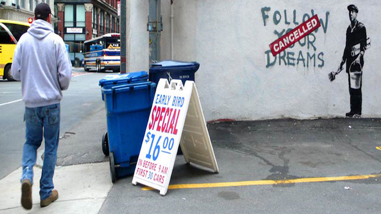 Man walking along city street past mural saying 'follow your dreams cancelled'