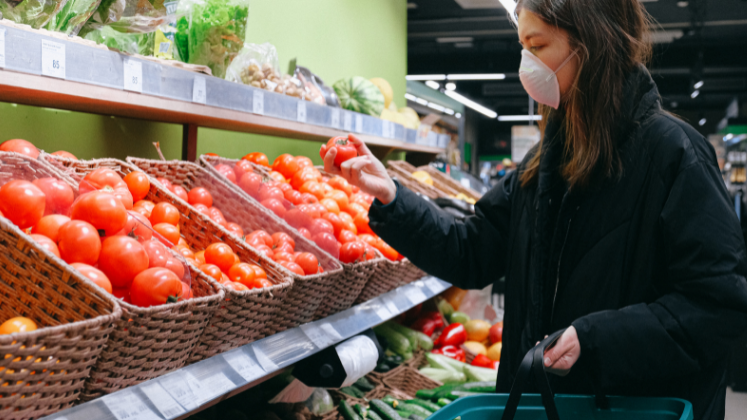 Woman in mask picking a tomato in grocery store_stock photo 747x420