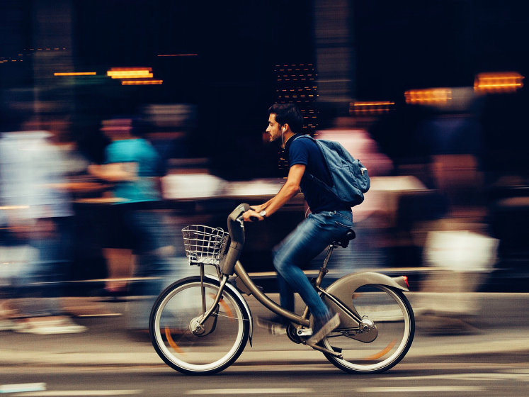 Man riding bike along busy city street_747x560_sourced via Canva