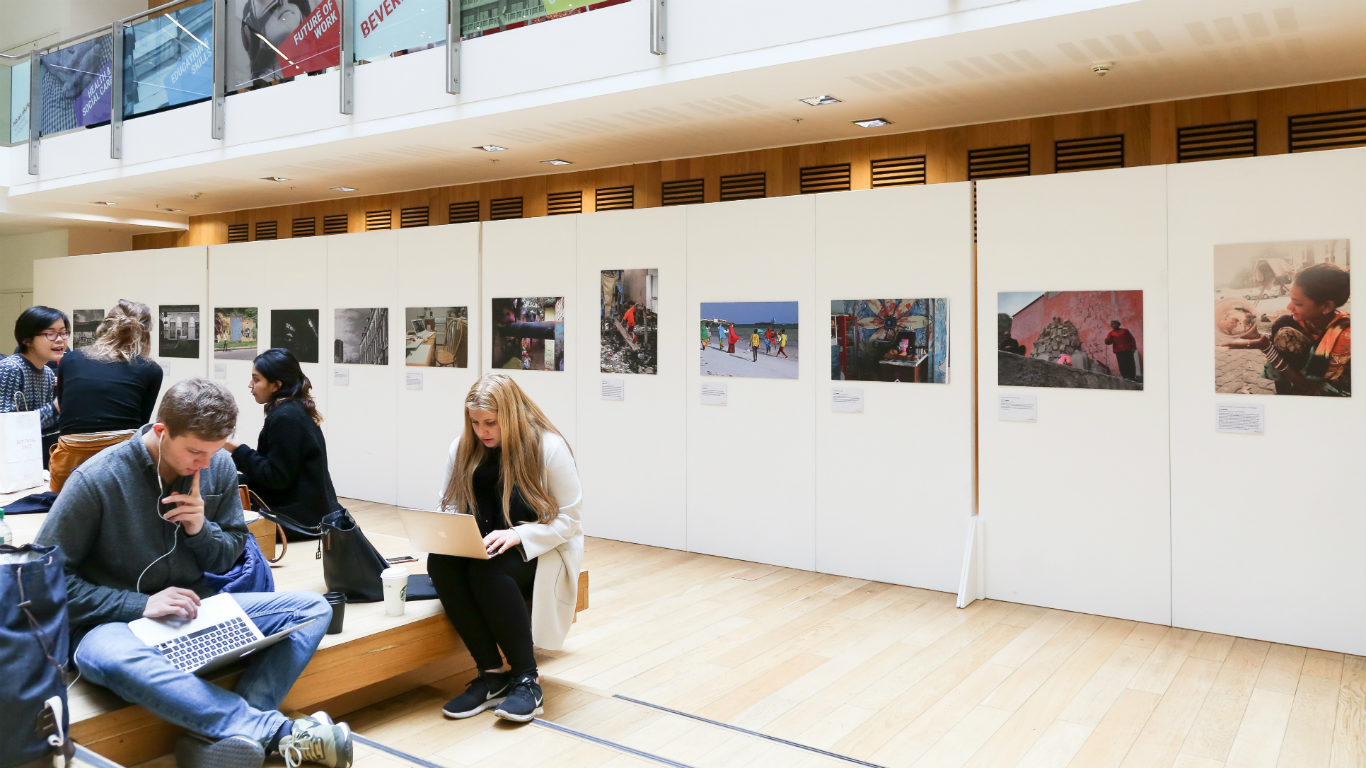 A gallery space with photographs displayed and students sitting around.