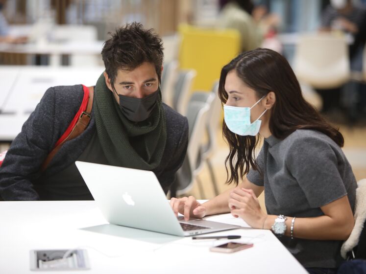 Two students, wearing masks, look at a laptop together in the study area of LSE's Centre Building, 2020. LSE/Nigel Stead.