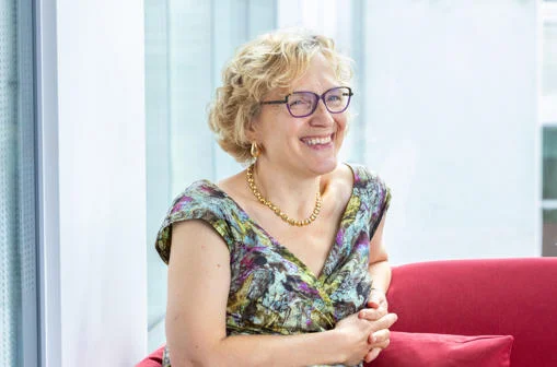 Elizabeth Holden, a blonde woman in glasses, smiling beyond the camera