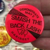 A pink and black badge with SMASH THE BACK LASH written on it