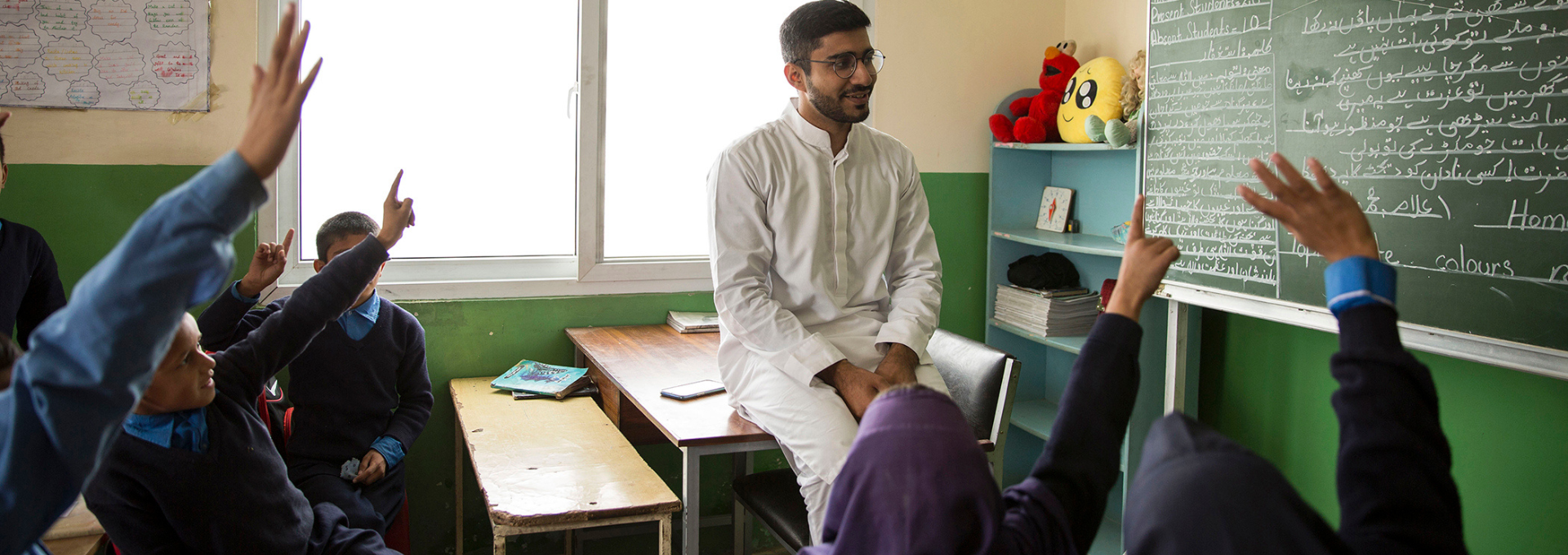 Teacher sitting on a desk in front of students with raised hands