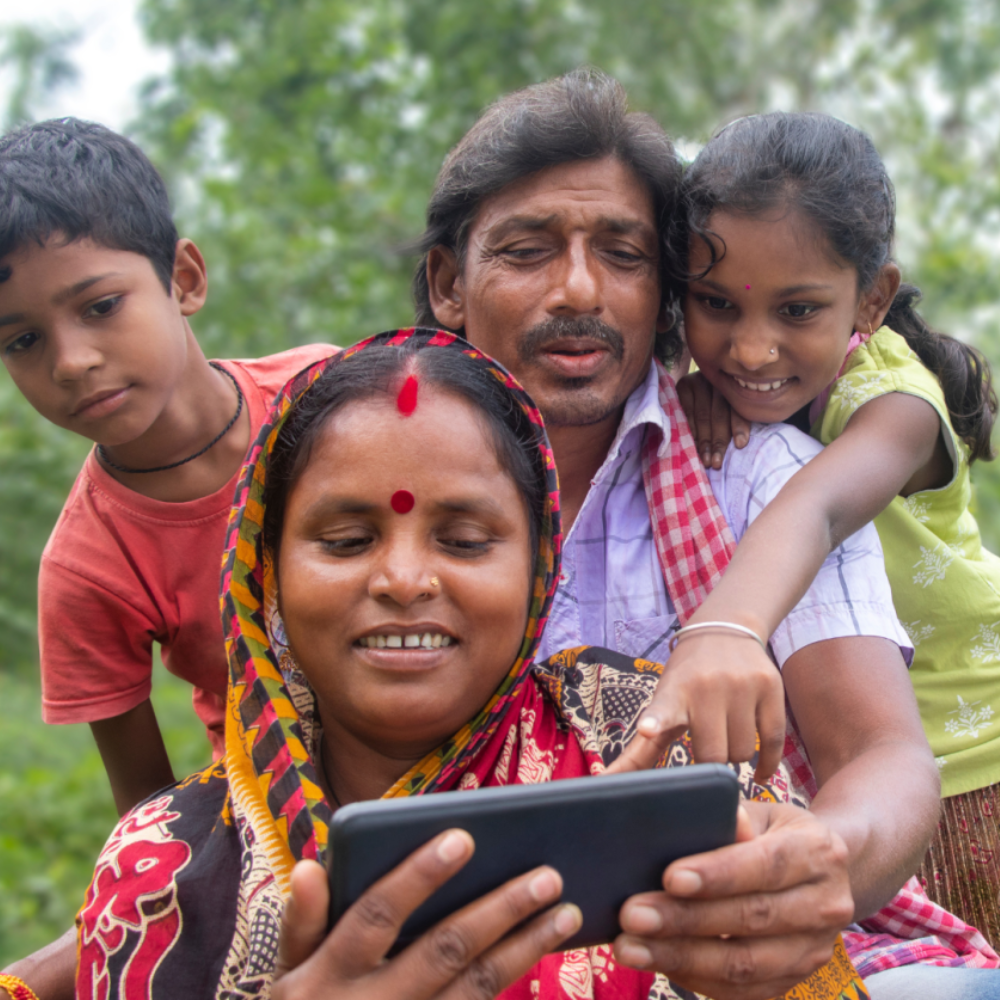 Woman holds a phone with a man and two children looking at it over her shoulder