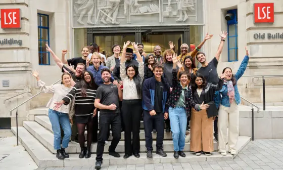 A group of people posing with their arms raised on the steps of the LSE OLD building