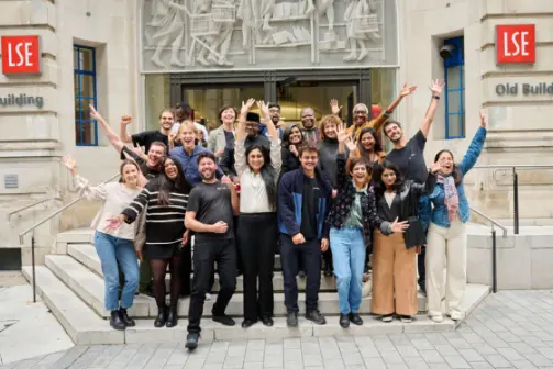 A group of people posing with their arms raised on the steps of the LSE OLD building
