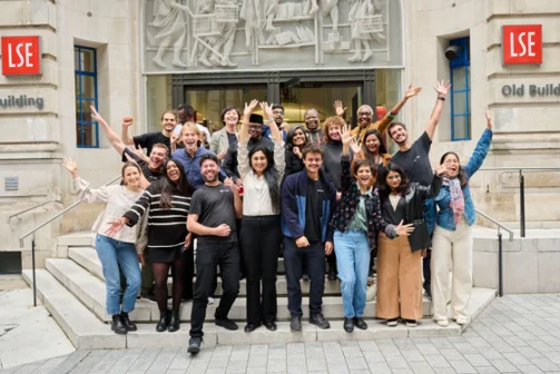 A group of people posing with their arms raised on the steps of the LSE OLD building