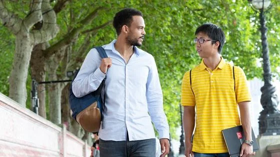 Two students in conversation while walking along a tree lined street