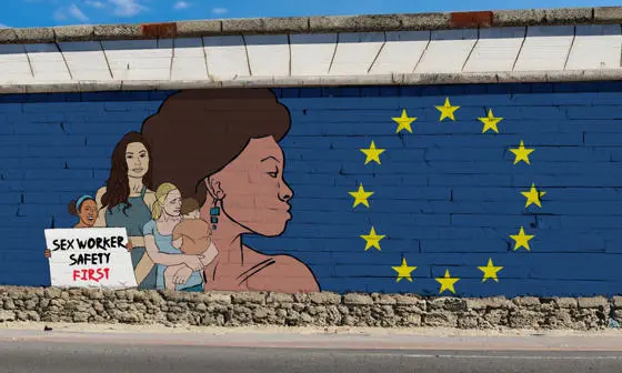 A mural on a blue brick wall features women and the EU flag. One woman holds a sign reading, "sex worker safety first"