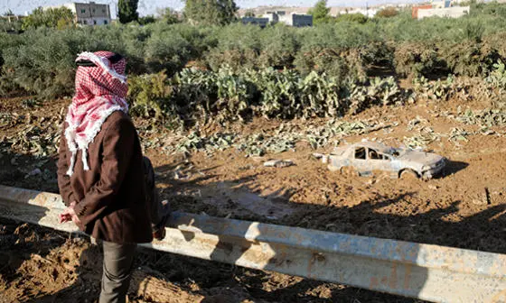 A person stands looking at a car half submerged by floods in Jordan.