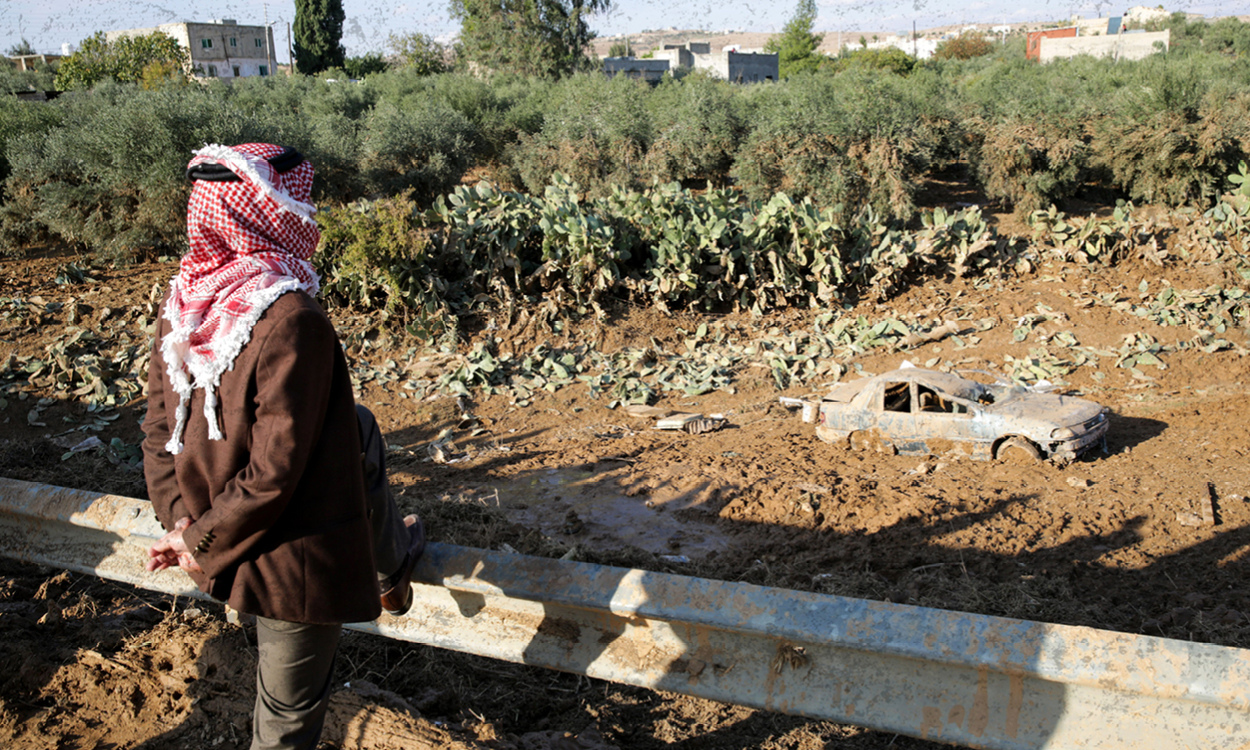 A person stands looking at a car half submerged by floods in Jordan