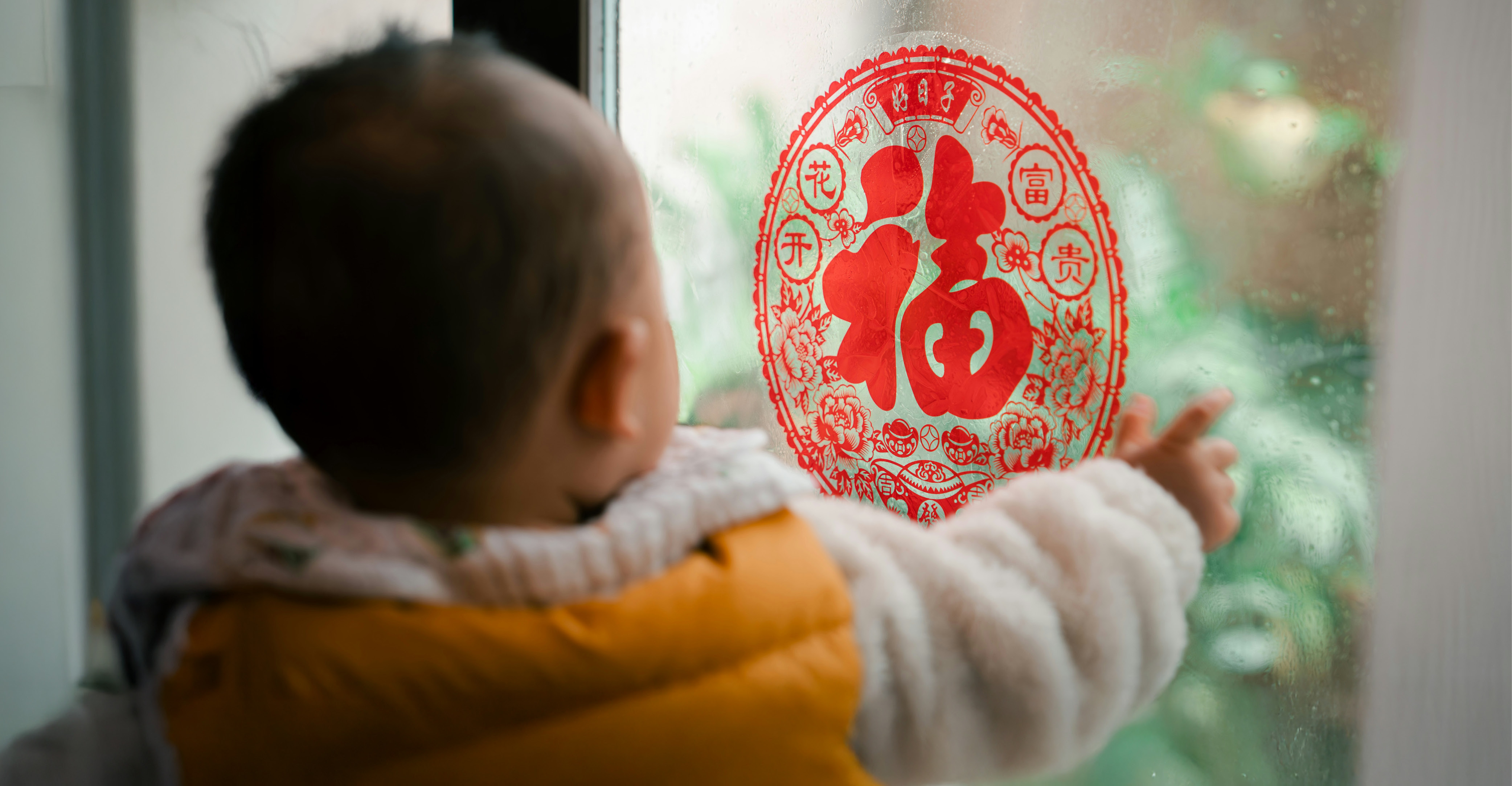 Child facing a window with Chinese decoration