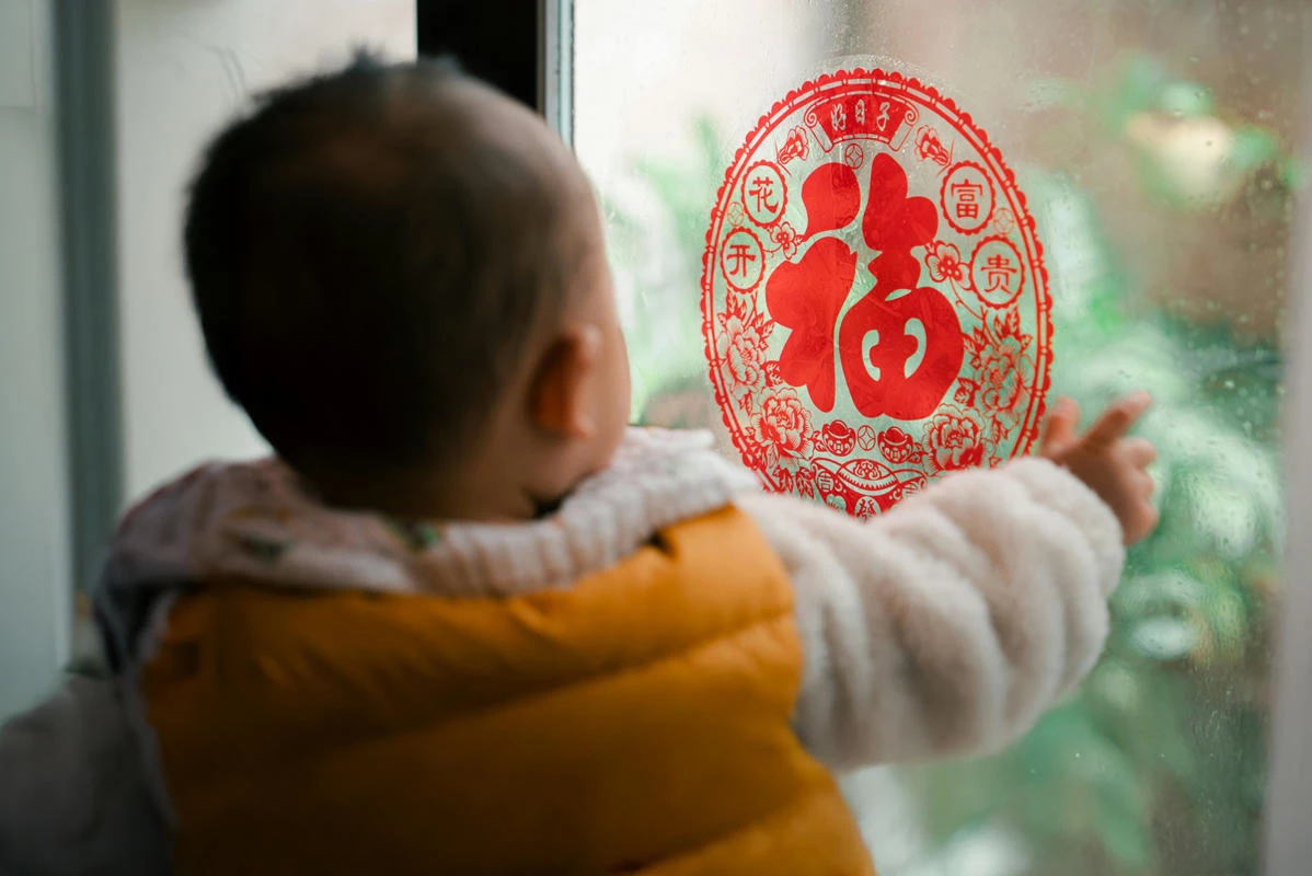 Child facing a window with Chinese decoration