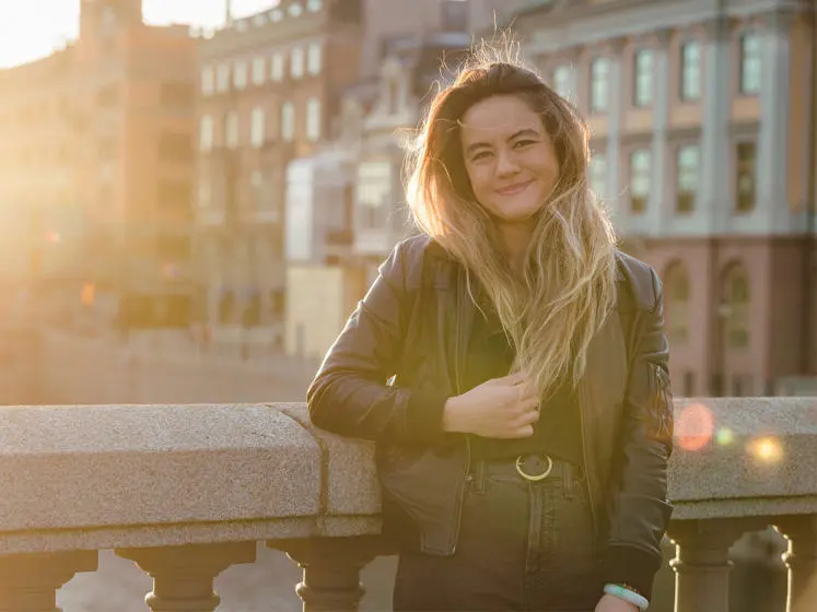 April Stephenson stands on a bridge in a city during sunset