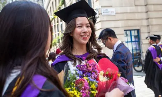 Young graduate in robes and holding bouquets