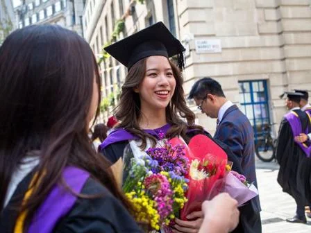 Young graduate in robes and holding bouquets