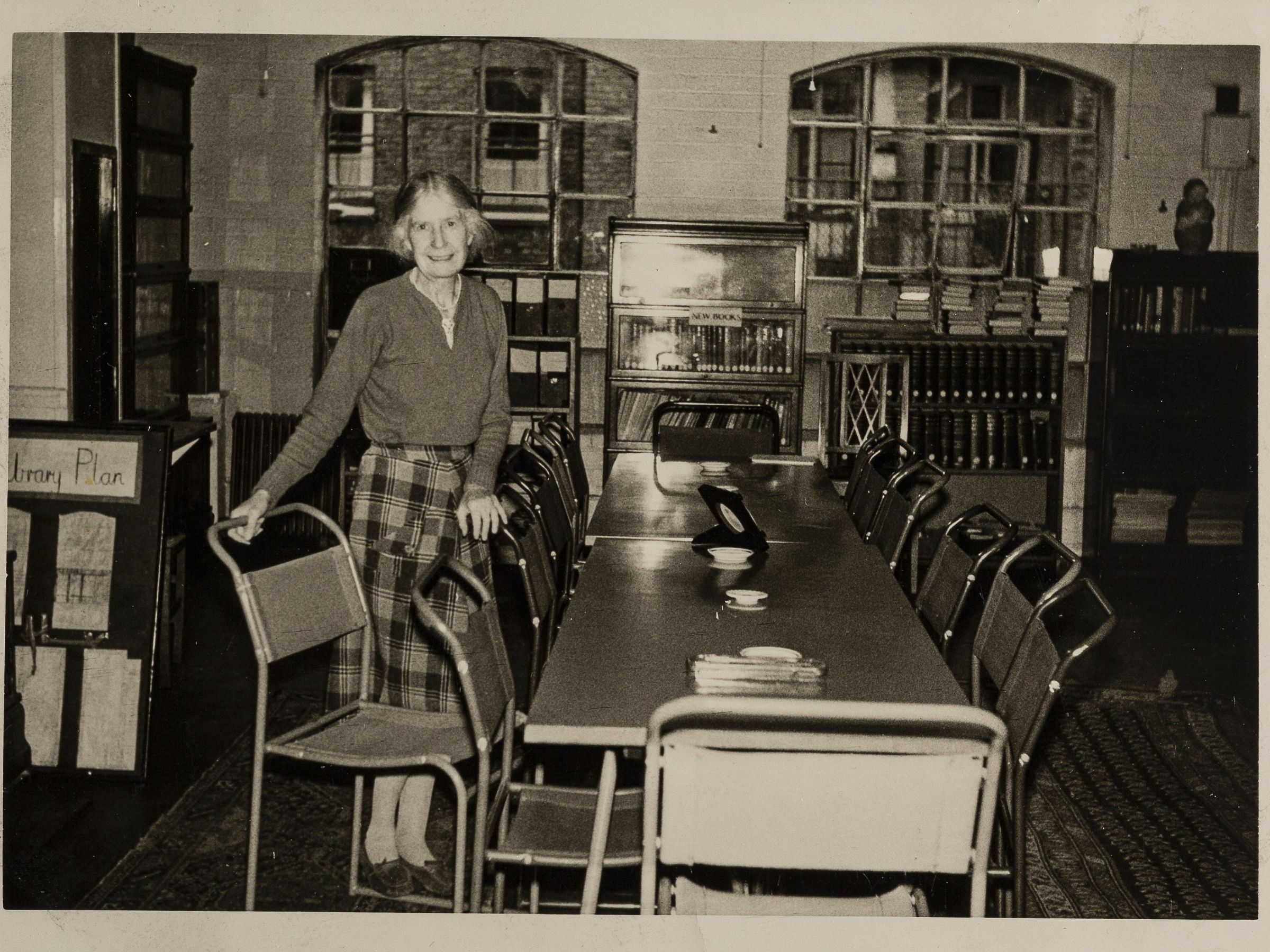 A person stood at a long desk pulling one of the chairs away from the table.