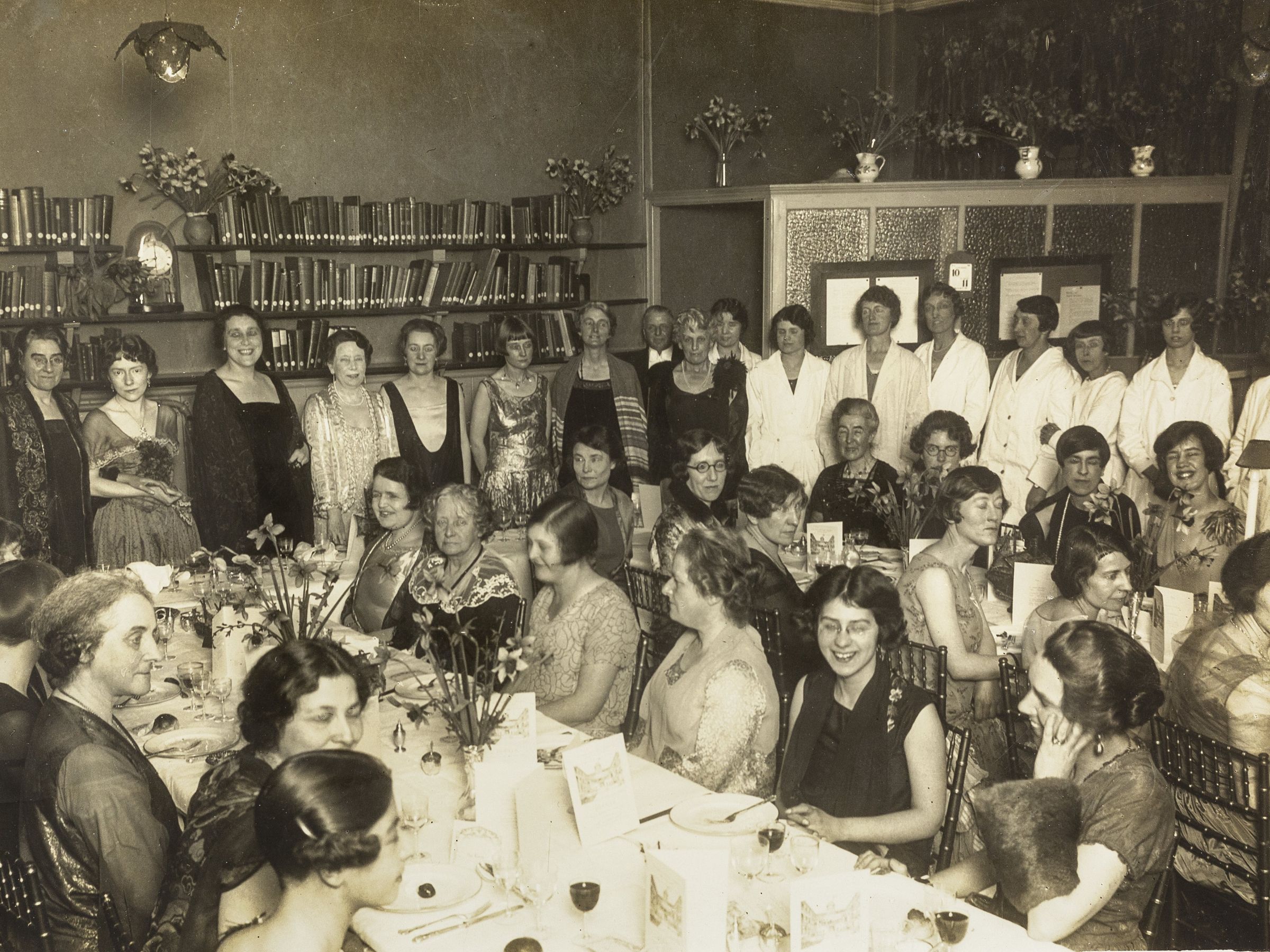 A large group photo, some people stood and others sat at dressed tables.
