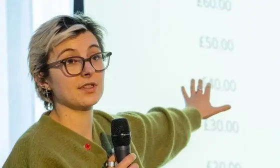 A woman stands in front of a screen with a microphone