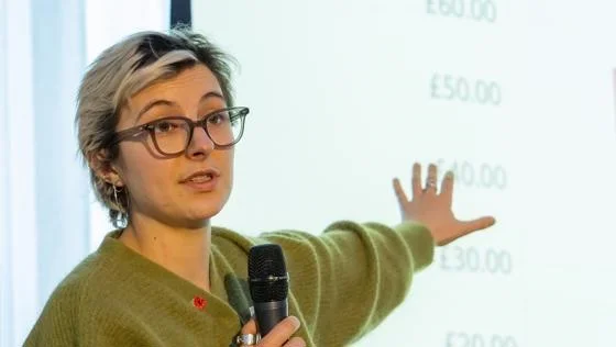 A woman stands in front of a screen with a microphone