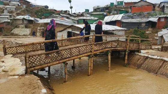 Women walking over a bamboo bridge in a refugee camp.