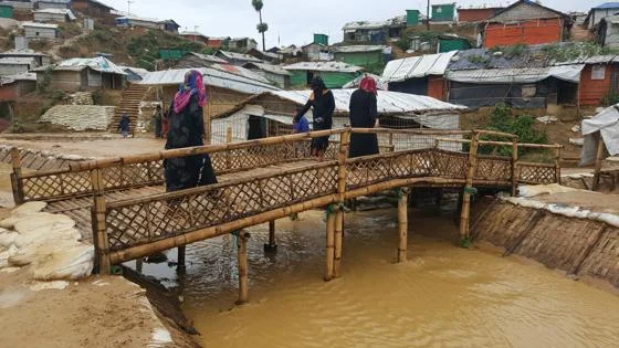 Women walking over a bamboo bridge in a refugee camp.