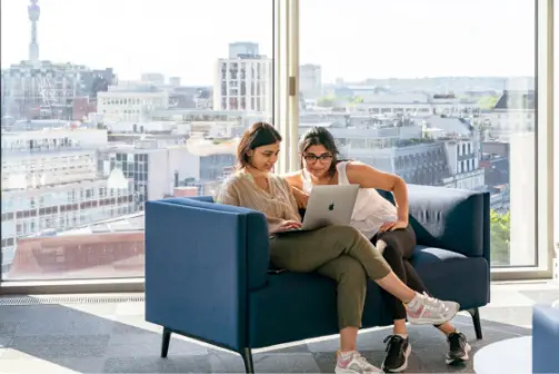 Two women sit in LSE's Centre Building looking at a laptop