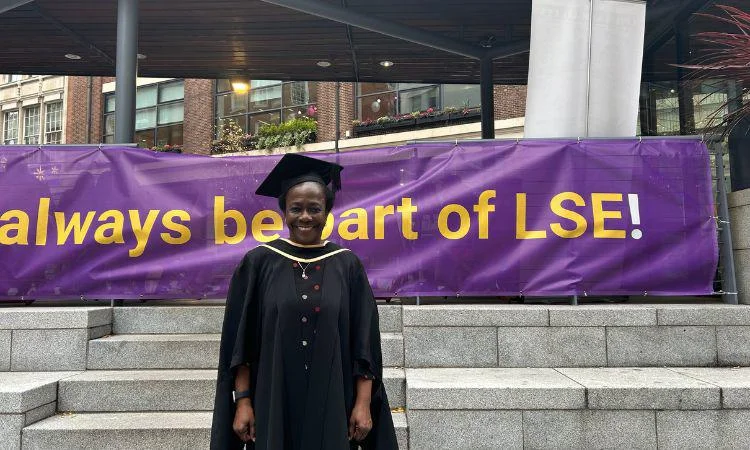 Alumna Abimibola Akinyemi standing in front of purle LSE banner on plaza