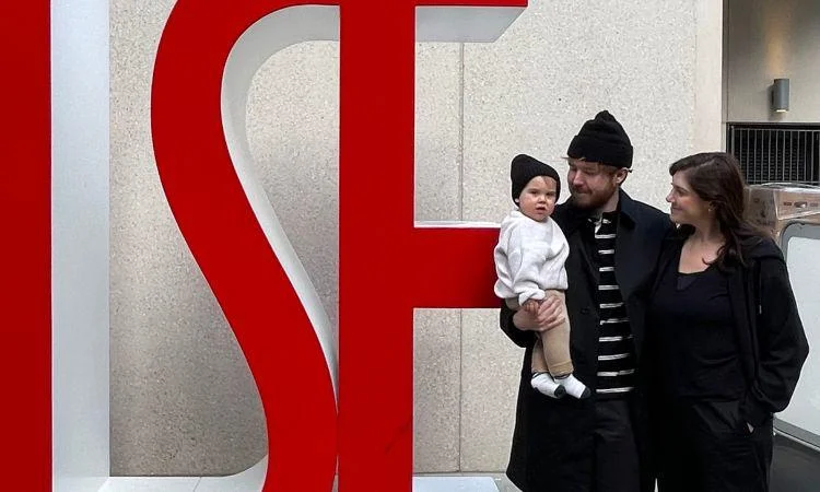 Alumni Selbi Sasioglu and Jake Fryer with their baby in front of LSE letters