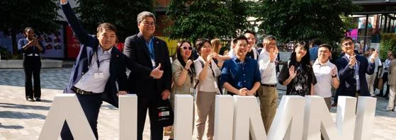 Group of alumni in front of alumni letters on plaza