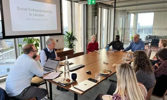 Group of people sitting around a table listening to a presentation