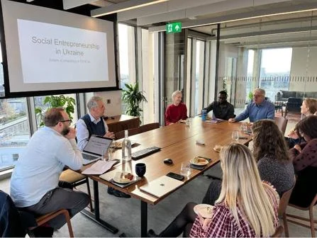 Group of people sitting around a table listening to a presentation