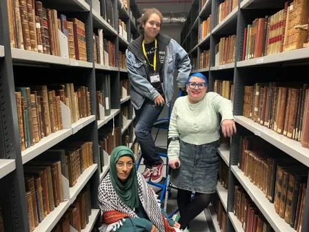 Three people posing between two book shelves